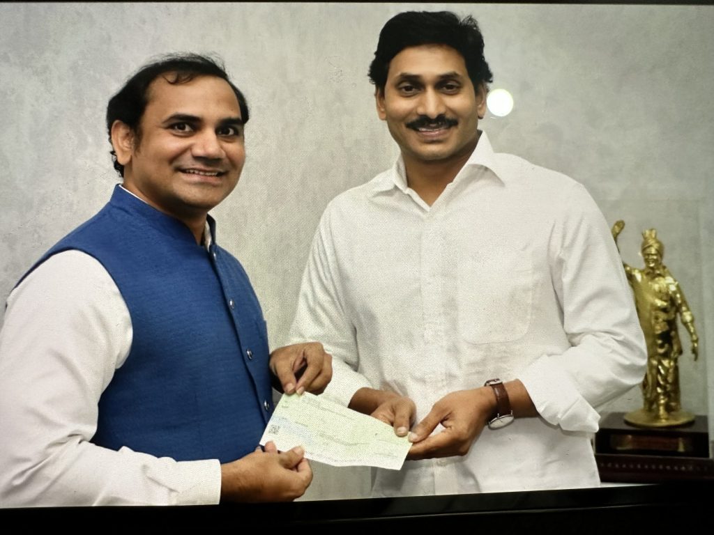 Y. S. Jagan Mohan Reddy in a white shirt smiling as he receives a cheque from a donor