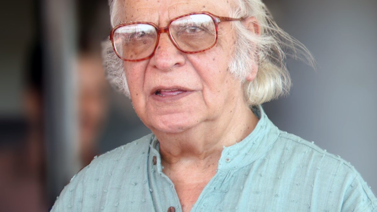Yash Pal with white hair and glasses, in a pale kurta, speaking