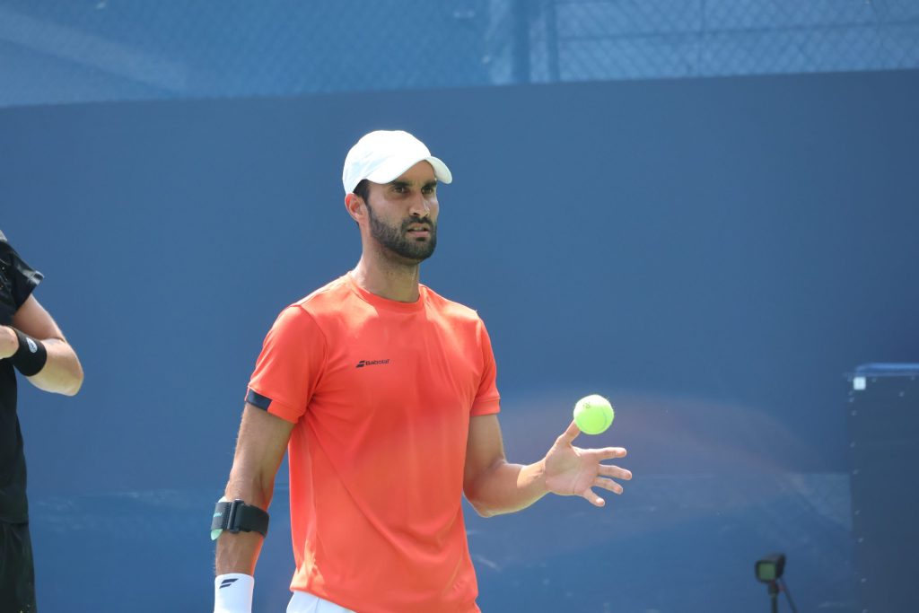 Yuki Bhambri in an orange shirt and white cap preparing to serve