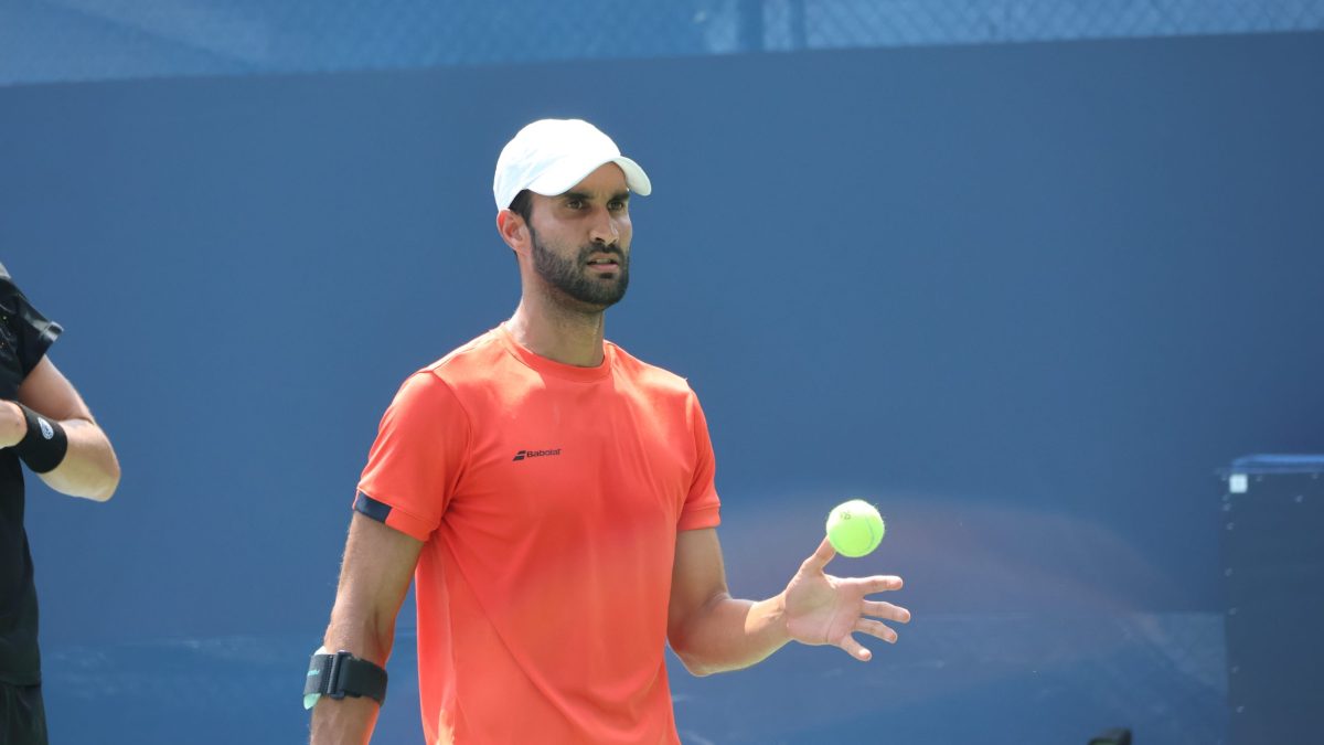 Yuki Bhambri in an orange shirt and white cap preparing to serve