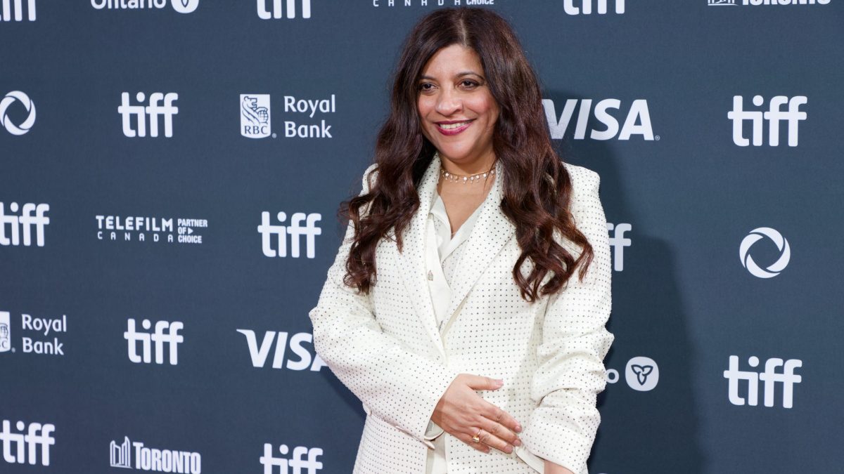 Zoya Akhtar in a white suit smiling in front of a TIFF backdrop